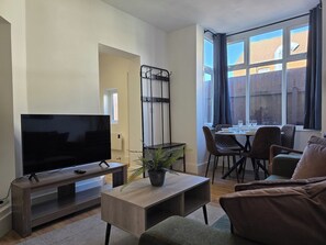 A modern living room with a flat-screen TV, a coffee table, and a dining area with chairs and a table. - Modern Apartment w/ Free Parking & Fast WiFi (Gloucestershire)