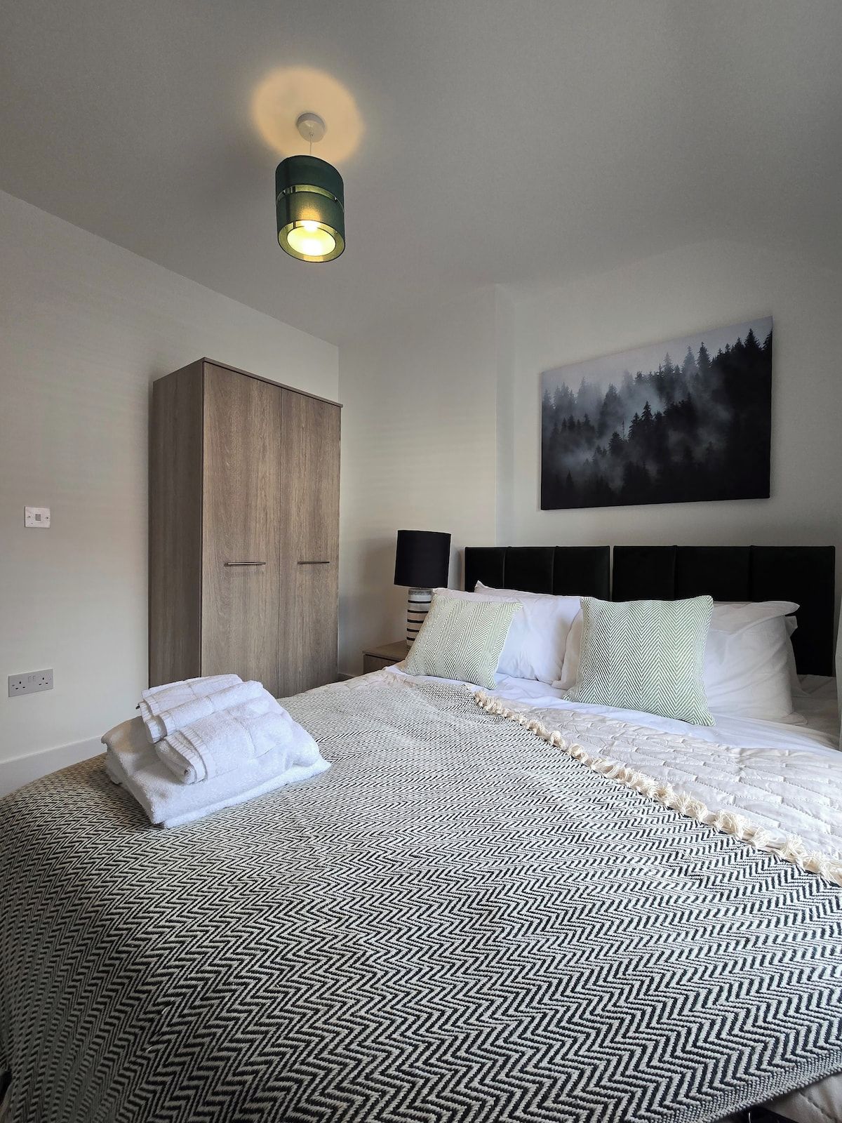 Una cama bien hecha con una colcha estampada, un cabecero con una obra de arte con motivos forestales y un armario de madera.
