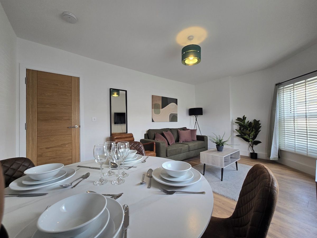 En matplats med ett runt bord för fyra personer, en soffa, en golvlampa och ett fönster med persienner.