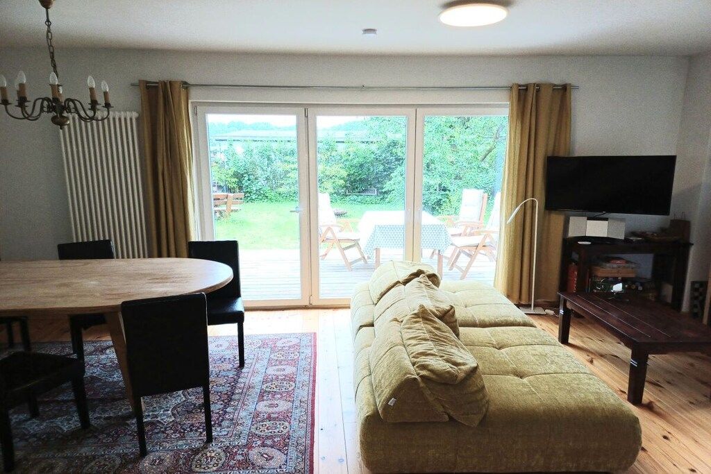A living room with a sofa, a TV, a dining table with chairs, and a view through a glass door to an outdoor area.