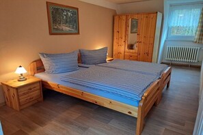 Puisesta sängystä, jossa on pääty, yöpöytä lampun kanssa ja vaatekaappi.