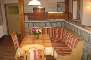 Ein Essbereich mit Tisch, Stühlen, einer Bank, einer Blumenvase und einer Küche im Hintergrund.