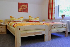Ein Doppelbett aus Holz mit einer gestreiften Decke und Kissen, ein Nachttisch mit einer Lampe, ein Fenster mit Vorhängen und eine Heizung.
