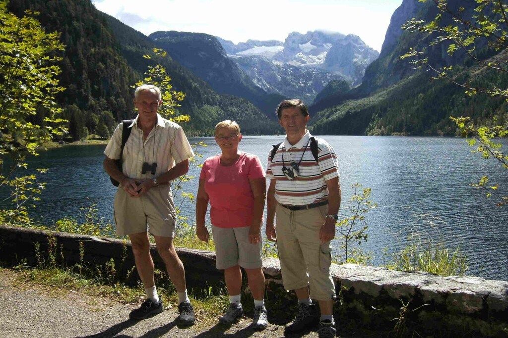 Three people standing by a lake with mountains in the background.