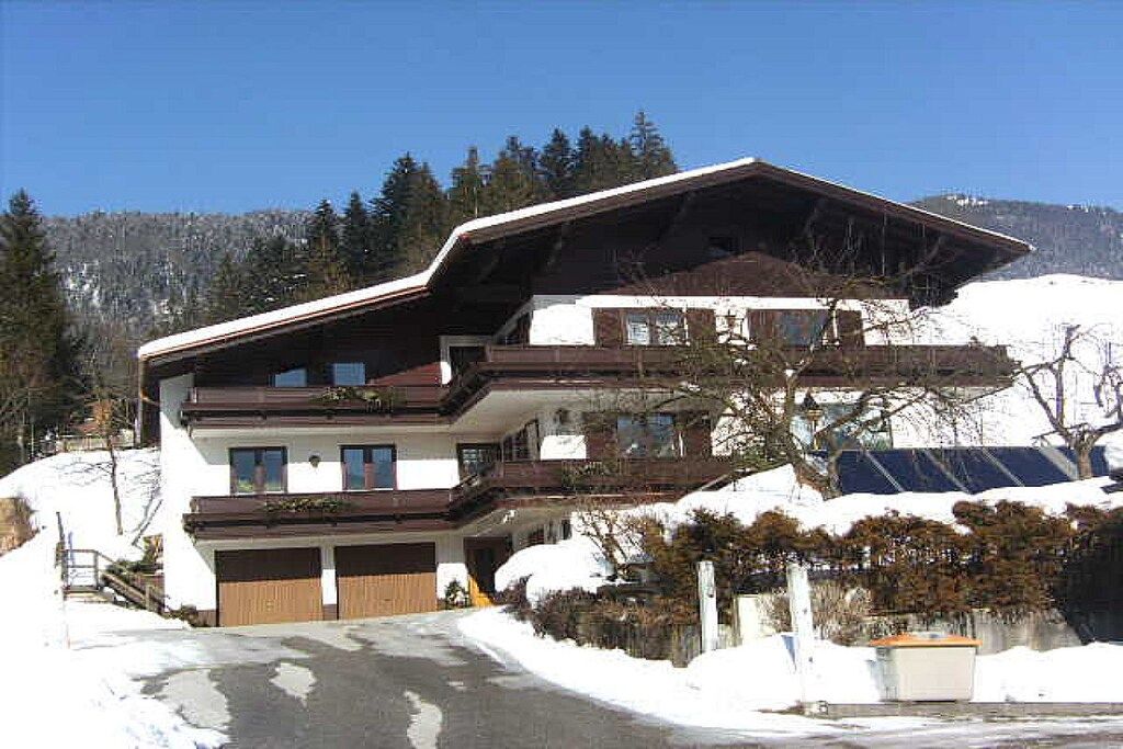 Um edifício de vários andares com telhado inclinado, garagem e vista para uma paisagem nevada.