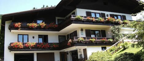 Un immeuble à plusieurs étages, doté de balcons ornés de fleurs, d’une entrée couverte et d’une voiture garée devant.