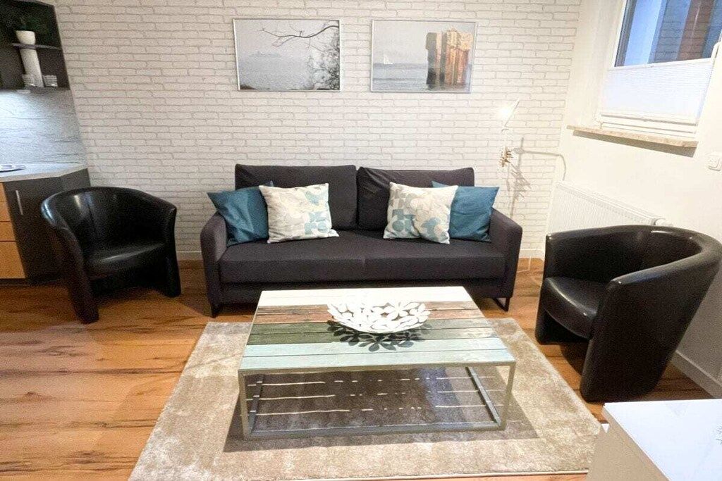 Un salon comprenant un canapé, deux fauteuils, une table basse en verre et un mur en briques orné de deux tableaux encadrés.