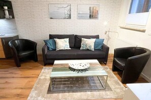 Ein Wohnzimmer mit einer Couch, zwei Sesseln, einem Glastisch und einer Ziegelwand mit zwei gerahmten Bildern.