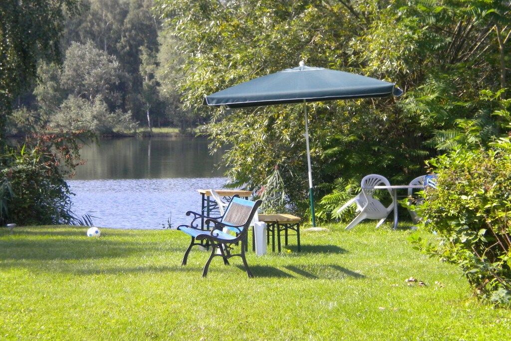 A grassy area with a bench and a table, a green umbrella, and a lake in the background.