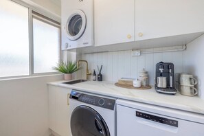 Een kleine keuken met een wasmachine, een koffiezetapparaat en een spoelbak.