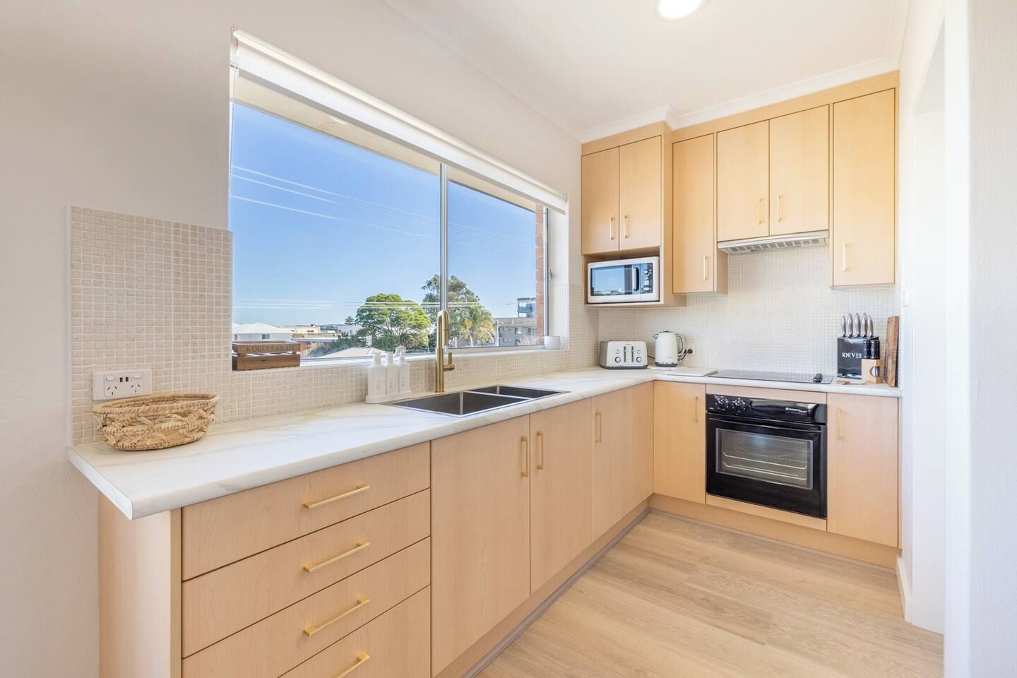 A modern kitchen with a large window, wooden cabinets, a microwave, a toaster, and a dishwasher.