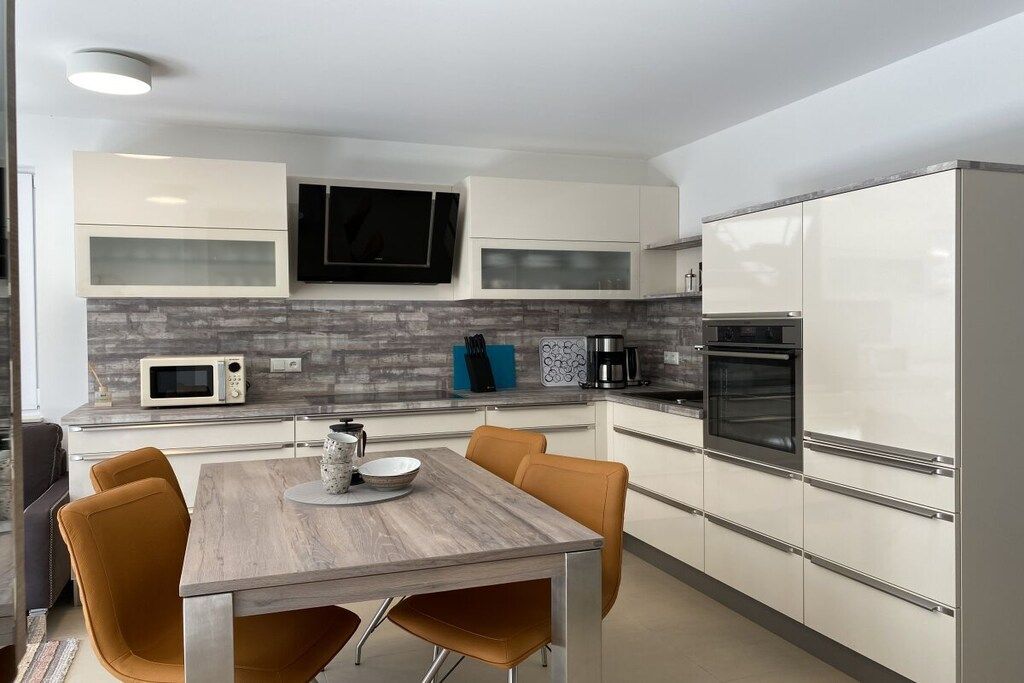 Cocina moderna con armarios blancos, microondas, cafetera y horno empotrado.