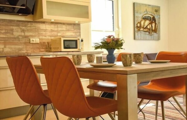 A dining area with a wooden table and four chairs, a vase with flowers, and a microwave on the counter. - Holiday home with 2 bedrooms (Ostseeheilbad Zingst)