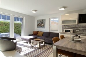 A modern living room with a sofa, coffee table, and dining table. There is a kitchen area with a microwave and cabinets. - Holiday home with 2 bedrooms (Ostseeheilbad Zingst)