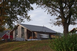A two-story building with a sloped roof, a covered porch, and a boat docked outside. - Holiday home with lake view (Rheinsberg)