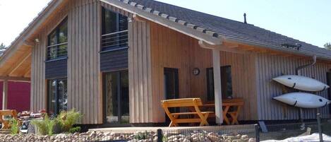 A wooden cabin with a covered patio, a pool, and two kayaks.