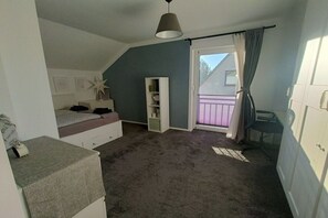 Ein Schlafzimmer mit Bett, Schreibtisch, Stuhl, Kleiderschrank und einem Fenster mit Vorhängen.