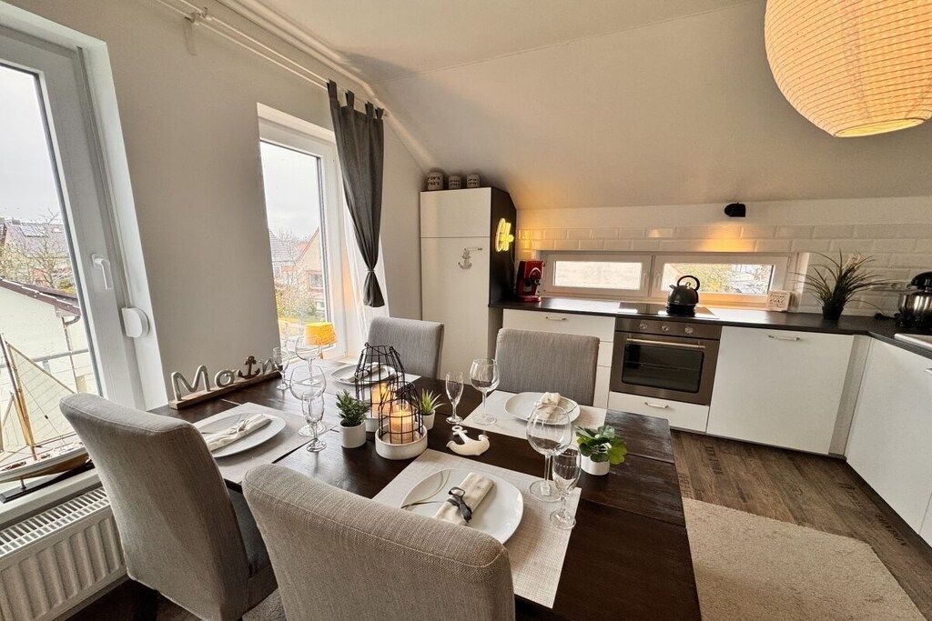 Une cuisine moderne avec des meubles blancs, un coin repas avec des chaises grises et une vue sur l’extérieur.