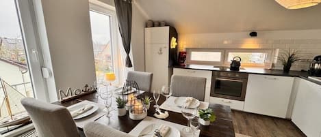 Una cocina moderna con armarios blancos, un comedor con sillas grises y vistas al exterior.