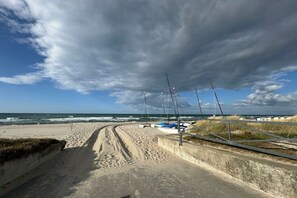 Eine Küstenstraße mit Sandstrand, einem Metallzaun und einigen Segelbooten.