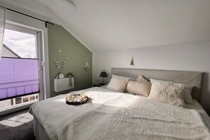 Ein Schlafzimmer mit einem großen Bett, einem Fenster mit Jalousien, einem Nachttisch und einem Wandregal.