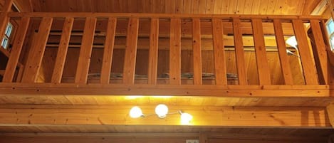 A wooden interior with a balcony, a ceiling light fixture, and a television.