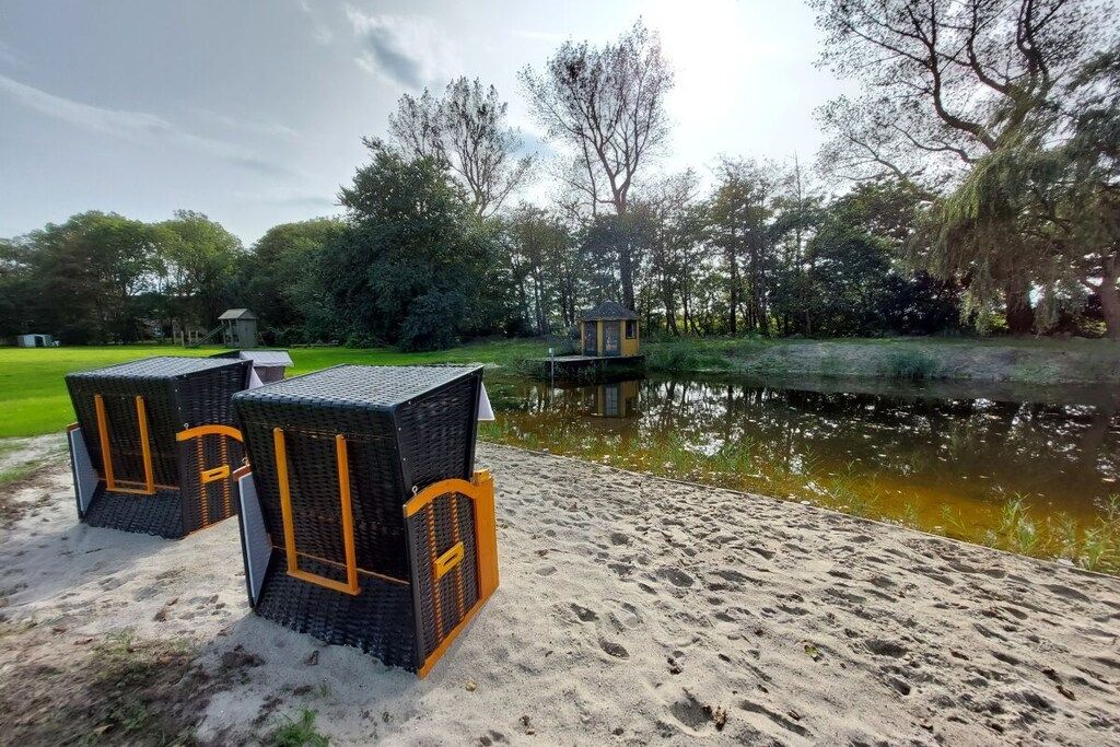 Korbmöbel im Freien neben einem Teich, umgeben von Bäumen und einer kleinen Struktur.