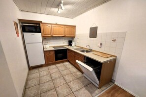 A compact kitchen with wooden cabinets, a built-in oven, a dishwasher, and a sink. - Holiday apartment with 1 bedroom (Butjadingen)