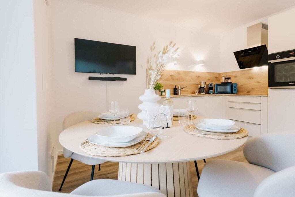 Ein moderner Essbereich mit einem runden Tisch für zwei Personen, einem an der Wand befestigten Flachbildfernseher und einer Küchenzeile mit Mikrowelle und Backofen.
