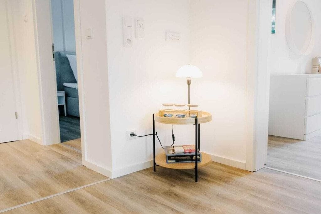 A room with a wooden floor, a round table with a lamp, and a white wall.
