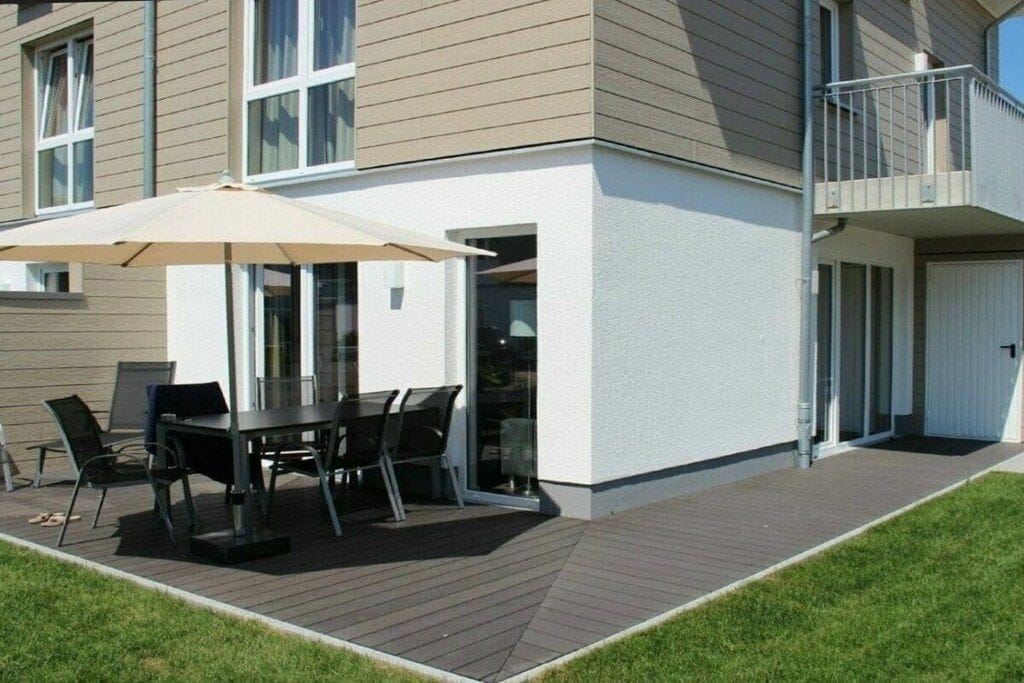 A modern building with a patio area featuring a table and chairs, a glass door entrance, and a small balcony.