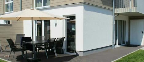 A modern building with a patio area featuring a table and chairs, a glass door entrance, and a small balcony.