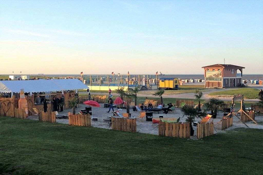 Eine Veranstaltung am Strand mit überdachtem Bereich, Sitzgelegenheiten und einem Rettungsturm.