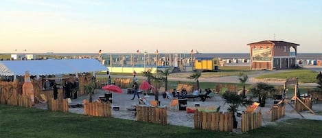Eine Veranstaltung am Strand mit überdachtem Bereich, Sitzgelegenheiten und einem Rettungsturm.