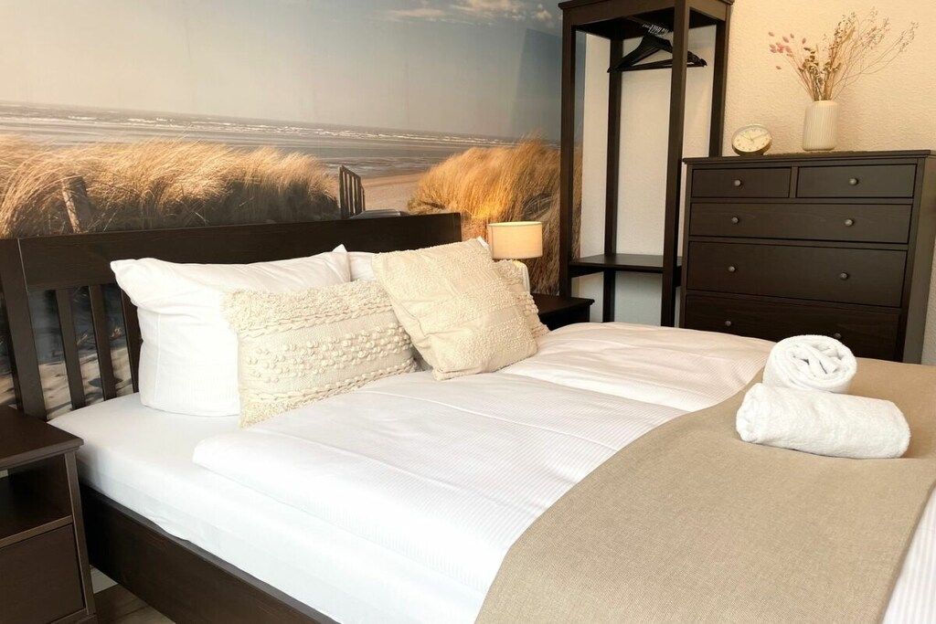 Una camera da letto con un letto, un comodino, una cassettiera e un affresco raffigurante una spiaggia.
