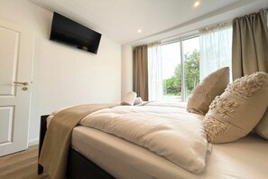 Een slaapkamer met een bed, een aan de muur bevestigde televisie en een raam met gordijnen.