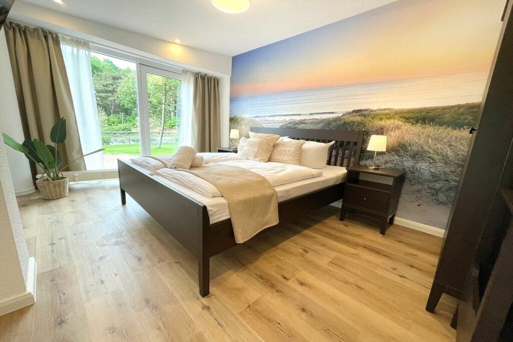 Un dormitorio con una cama grande, una mesita de noche, una lámpara y vistas al exterior a través de una ventana.