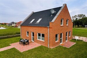 A two-story brick house with a sloped roof, satellite dish, and a patio with outdoor furniture. - Holiday home with 3 bedrooms (Greetsiel)