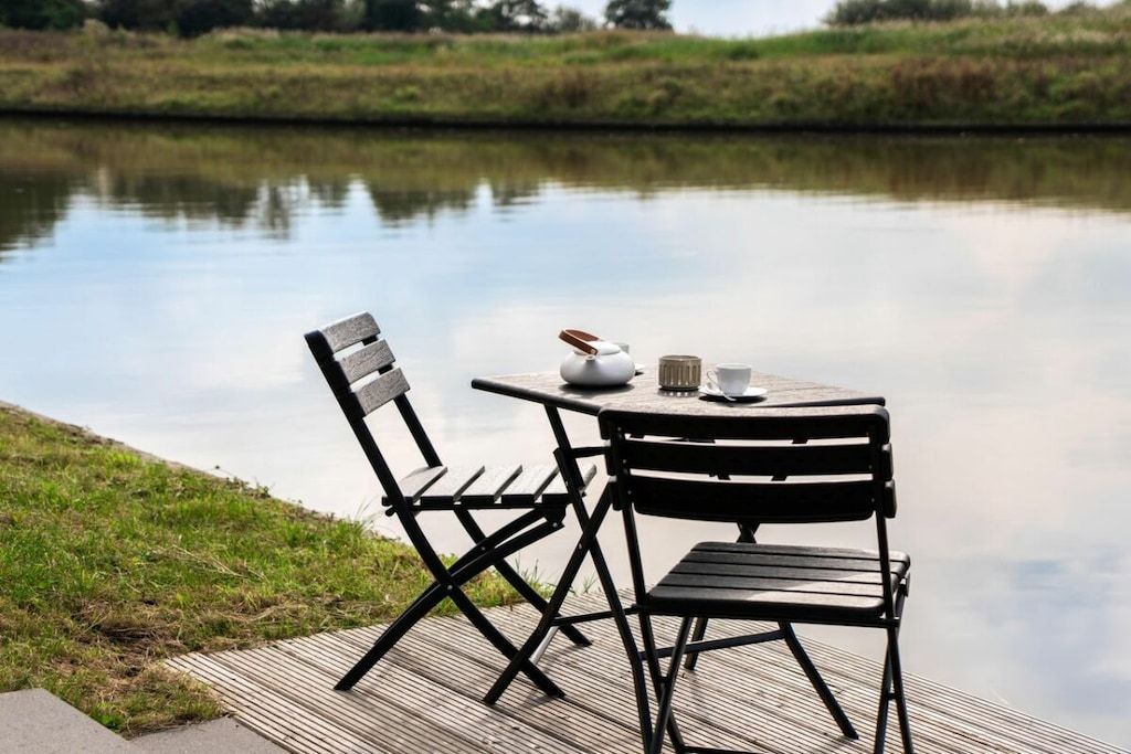 A tranquil outdoor seating area with a table and two chairs by a calm body of water.