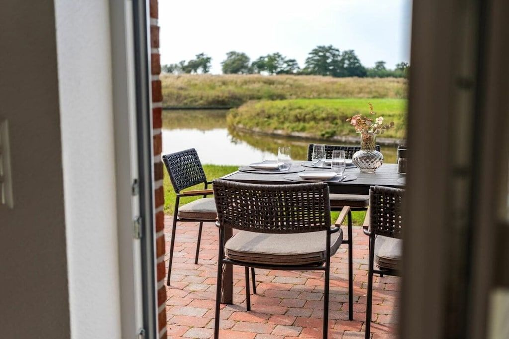 An outdoor dining area with a table set for two, chairs, and a vase with flowers.