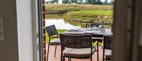 An outdoor dining area with a table set for two, chairs, and a vase with flowers.