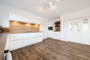 A modern kitchen with white cabinetry, a wooden countertop, and a built-in microwave. - Holiday home with 3 bedrooms (Greetsiel)