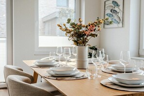 A dining table set with white plates, glasses, and cutlery, with a vase of flowers on the table. - Holiday home with 3 bedrooms (Greetsiel)