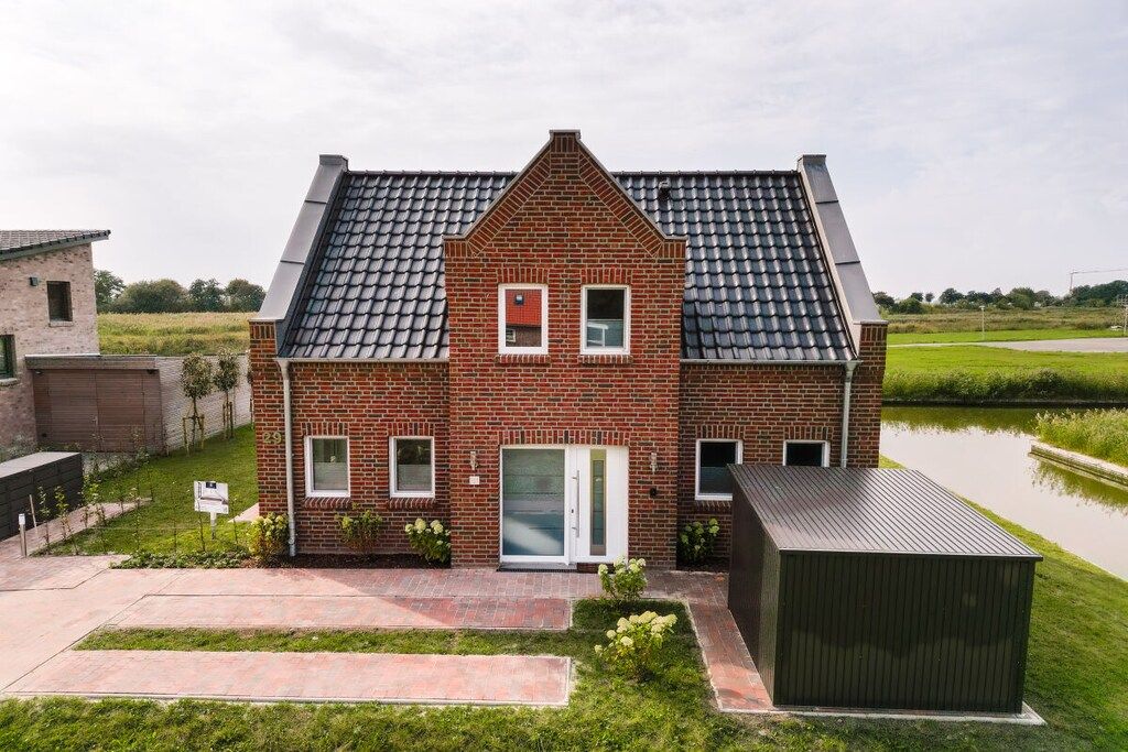 Une maison à deux étages, construite en briques, avec un toit en pente, une porte d’entrée et un petit garage attenant.