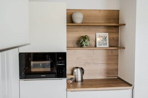 A kitchen with a built-in microwave, a kettle, and wooden shelves with decorative items. - Holiday home with 3 bedrooms (Greetsiel)