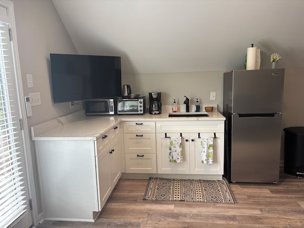 A compact kitchen with a microwave, toaster, coffee maker, and a refrigerator.