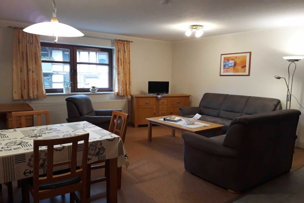 A living room with a sofa, a dining table with chairs, a television on a stand, and a window with curtains.