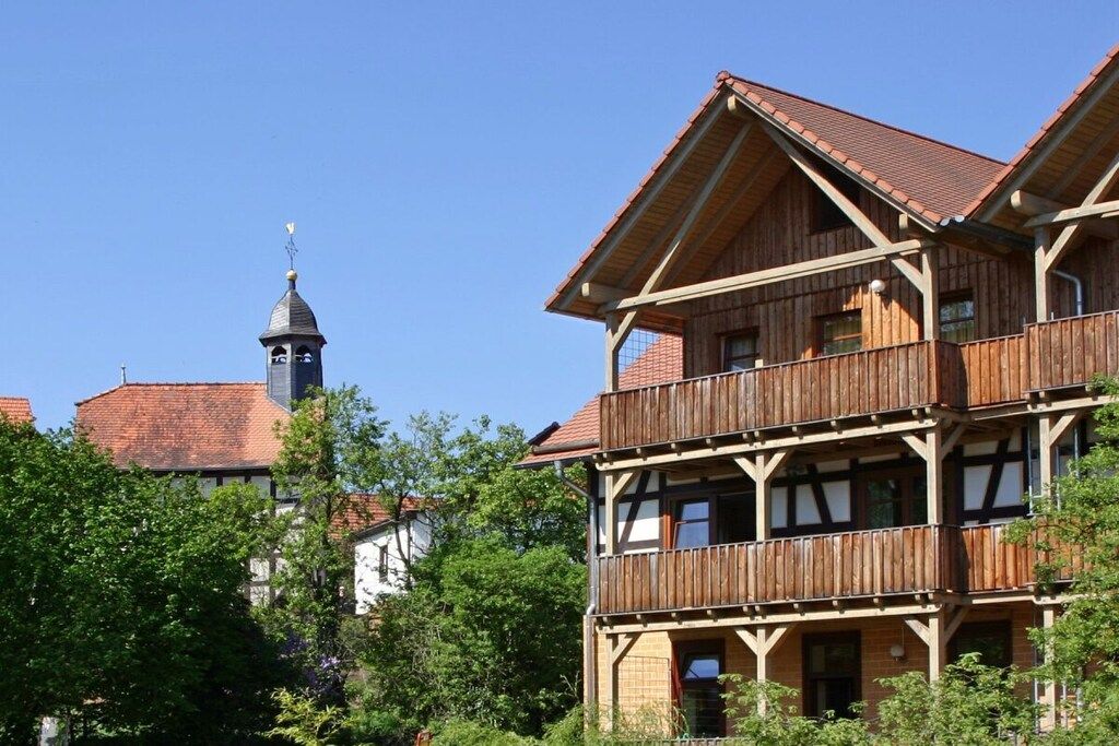 A multi-story wooden building with a balcony, surrounded by greenery.