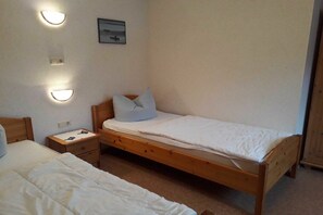Una habitación pequeña y sencilla con dos camas individuales, una mesita de noche e iluminación en la pared.