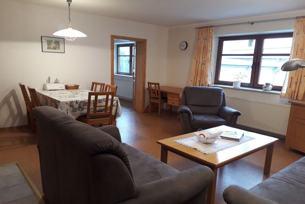 A living room with a sofa, a coffee table, a dining table with chairs, a chair, and a window with curtains.